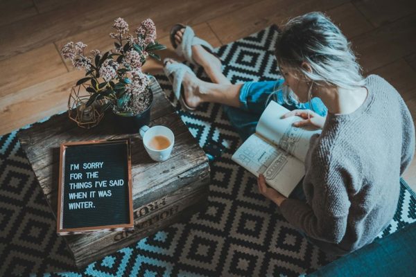 woman sitting on rug while reading book near tea table