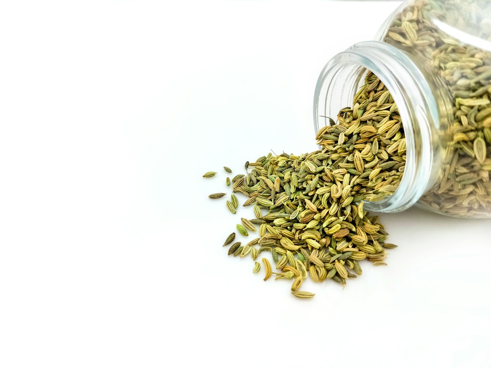 a glass jar filled with seeds on top of a white table. Fenchelsamen Fencheltee